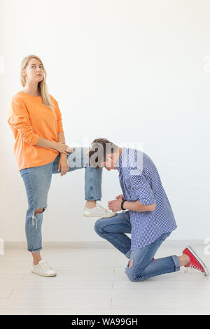 Young man is kneeling and reverently tying shoelaces to his domineering unidentified woman posing on a white background. Concept of dominant relations Stock Photo
