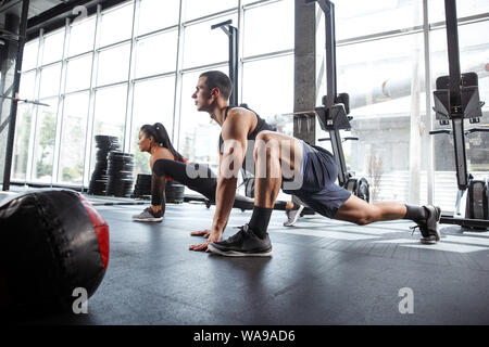 A muscular athletes doing workout at the gym. Gymnastics, training, fitness workout flexibility. Active and healthy lifestyle, youth, bodybuilding. Training in lunges and stretching exercises. Stock Photo