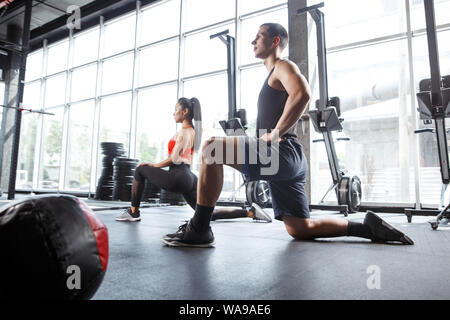 A muscular athletes doing workout at the gym. Gymnastics, training, fitness workout flexibility. Active and healthy lifestyle, youth, bodybuilding. Training in lunges and stretching exercises. Stock Photo