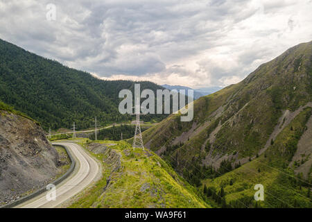 Asphalt road   with huge power transmission towers. Landscape with beautiful mountain road with a perfect asphalt. High rocks, amazing sky at sunset i Stock Photo