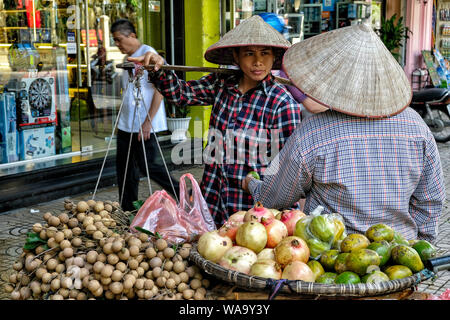 Hanoi, Vietnam - August 31: Street vendor carrying vegetables and fruit in baskets using a carrying pole on August 31, 2018 in Hanoi, Vietnam. Stock Photo