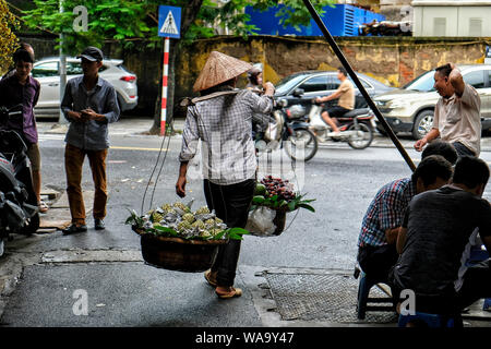 Hanoi, Vietnam - August 31: Street vendor carrying vegetables and fruit in baskets using a carrying pole on August 31, 2018 in Hanoi, Vietnam. Stock Photo