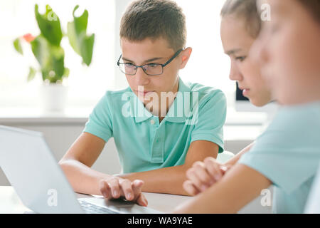 Two schoolboys concentrating on schoolwork while sitting in front of laptop Stock Photo
