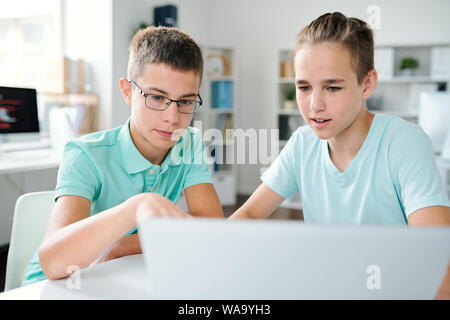 Two schoolboys discussing online data on laptop display at lesson Stock Photo