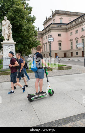 A young man on a Uber-owned LIME E-scooters on the sidewalk or pavement. E-Scooters have arrived recently in Berlin, Germany. Stock Photo