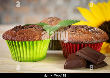 Muffins in colorful baskets with chocolate and sunflower on wooden table. Close up. Blurred foreground and background. Stock Photo
