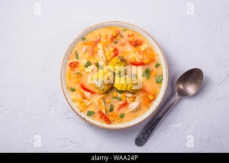 Mexican corn soup with pepper and chicken on a gray texture background with a spoon. Top view Stock Photo