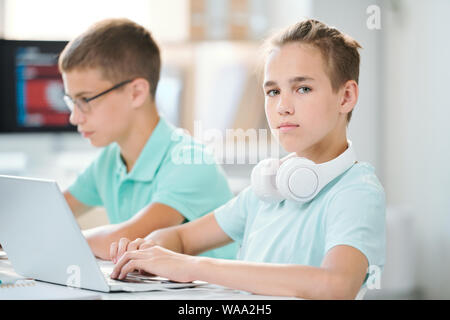 Cute and clever schoolboy with headpones on neck working over homework Stock Photo