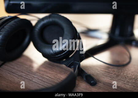 black headphones with a microphone on a wooden table near a computer. Workplace Stock Photo