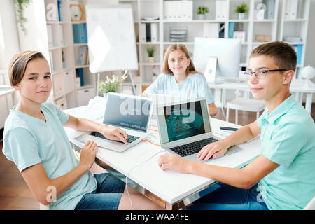 Three successful clever students of contemporary middle school sitting by desk Stock Photo