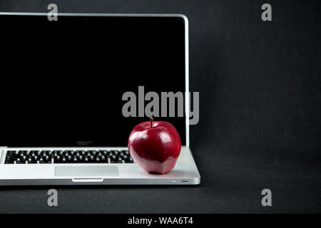 Shiny red apple resting on an open aluminum laptop in selective focus on a black background Stock Photo