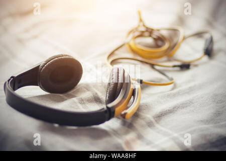 The yellow-black headphones with a long tangled wire lie on a soft gray plaid with white stripes, illuminated by sunlight. Stock Photo