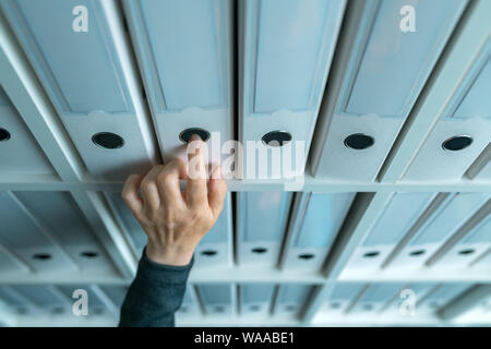 Businesswoman browsing through ring binder file documentation archives on the shelf in business office, close up of hand Stock Photo