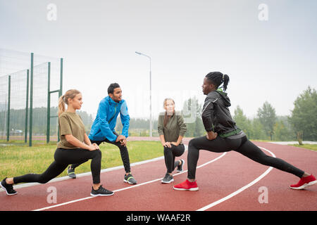 Four young friendly active people in sportswear exercising on racetracks