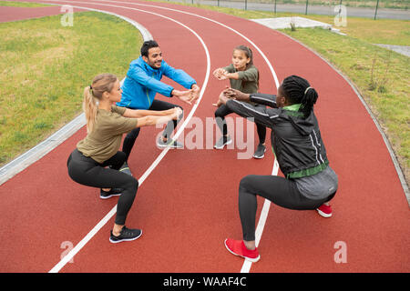 Young intercultural friends stretching their arms forwards while doing squats Stock Photo