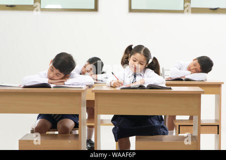 Sleeping students and diligent pupil in a school classroom Stock Photo
