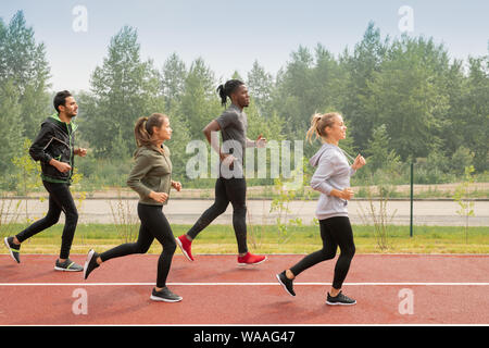 Side view of four young sportsmen and sportswomen running down racetracks Stock Photo