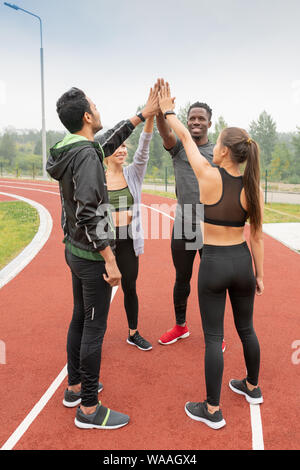 Intercultural friends in sportswear touching by hands while standing in circle Stock Photo