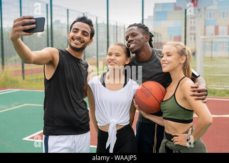 Group of young intercultural friends in sportswear making selfie on court Stock Photo