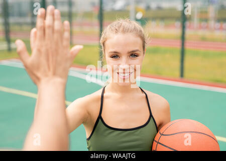 Pretty young blonde woman in activewear giving high-five to her friend Stock Photo