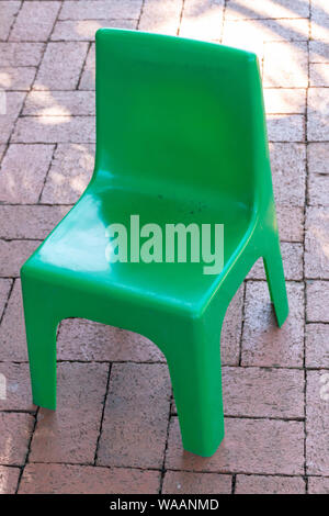 A close up front view of a green plastic chair on a brick pathway Stock Photo