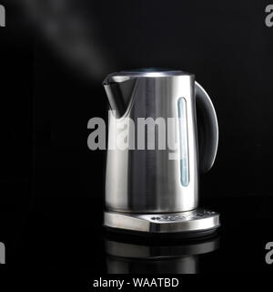 A modern kettle with steam on black reflective surface Stock Photo