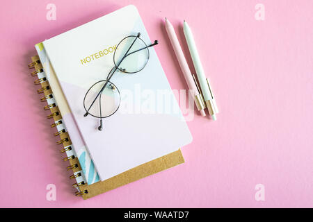 Overview of pink table with stack of notebooks, eyeglasses and two pens Stock Photo
