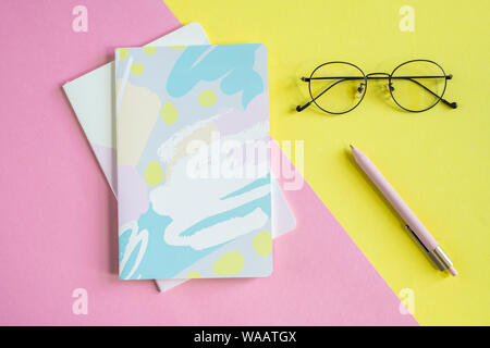 Eyeglasses and pen on yellow background and two notebooks on pink background Stock Photo