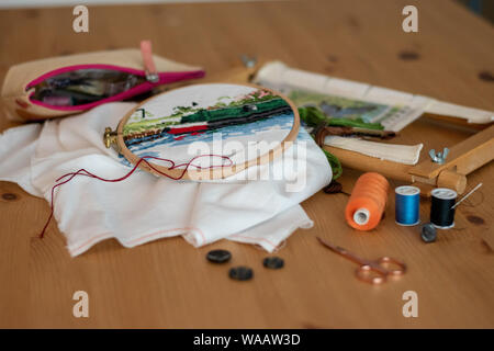 Cross-stitch embroidery materials, including threads, needles, scissors, linen and hoops. laid out on a table for craft/hobby Stock Photo