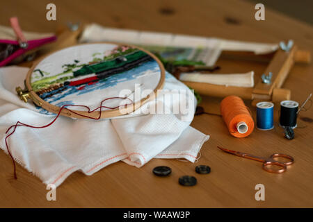 Cross-stitch embroidery materials, including threads, needles, scissors, linen and hoops. laid out on a table for craft/hobby Stock Photo