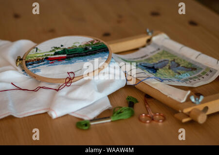Cross-stitch embroidery materials, including threads, needles, scissors, linen and hoops. laid out on a table for craft/hobby Stock Photo