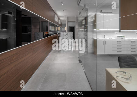 Modern illuminated interior of a dental clinic with light and textured brown walls and tiled gray floor. There is a reception desk, doors, cabinet wit Stock Photo