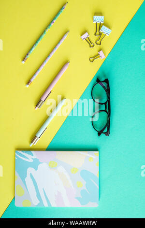Overview of pens, clips, notebook and eyeglasses on yellow and blue background Stock Photo