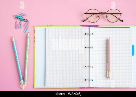 Open copybook with blank pages, pen, two pencils, clips and eyeglasses Stock Photo