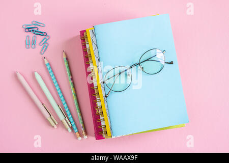Stack of notebooks with eyeglasses on top with clips, pens and pencils near by Stock Photo