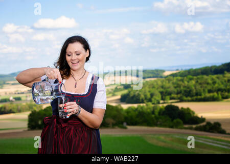 portrait of bavarian woman in dirndl standing in meadow with glass of water Stock Photo