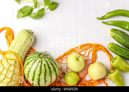 Green vegetables and fruits in orange reusable shopping mesh bag on white background: zucchini, cucumbers, bell pepper, hot peppers, apples, pear, wat Stock Photo