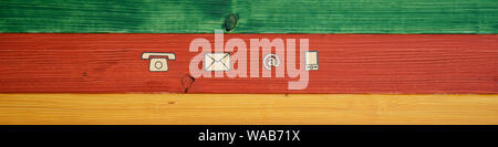 Wide view image of contact and communication icons cut out of paper placed in a row over a background of green, red and yellow wooden planks. Stock Photo