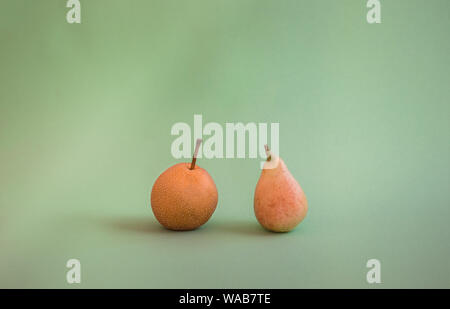Two different kinds of pears: Nashi or Asian pear and San Juan pear (type of small pear). Pears comparison. Fresh fruit isolated on green background. Stock Photo