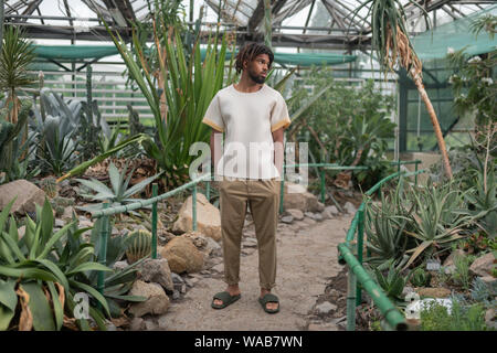 Stylish young man standing in the greenhouse with tropical plants Stock Photo
