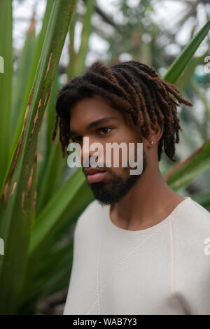 Serious dark-eyed young man posing in greenhouse Stock Photo