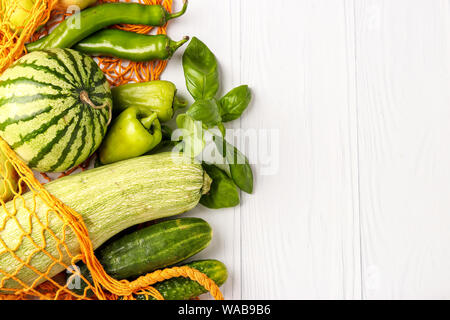 Green vegetables and fruits in orange reusable shopping mesh bag on white background: zucchini, cucumbers, bell pepper, hot peppers, apples, pear, wat Stock Photo