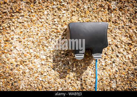 Domestic outdoor electrical outlet socket waterproof box with blue cable running from it. Stock Photo