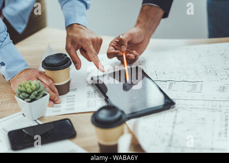 Close-up of a creative architects team using digital tablet while analyzing blueprints  of a new project in the office. Stock Photo