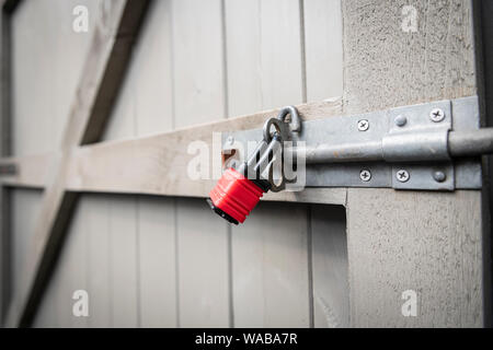 A red padlock securing a bolt on a grey garden gate. Stock Photo