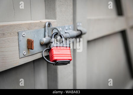 A red padlock securing a bolt on a grey garden gate. Stock Photo