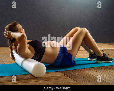 Pregnant woman in her thirties exercising in a gym doing situps. Stock Photo