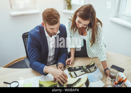 Two young architects working on a new project and communicating while analyzing blueprints in the office. Stock Photo