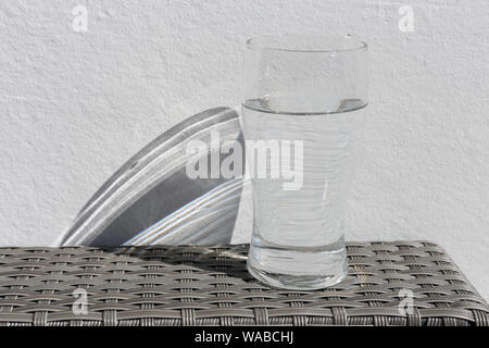 Big glass full of water photographed outdoors during a sunny summer day. White wall in the background. You can see a beautiful shadow too. Stock Photo