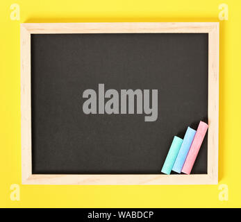Chalkboard with wooden frame and colorful chalks on one side, isolated on yellow background. Stock Photo